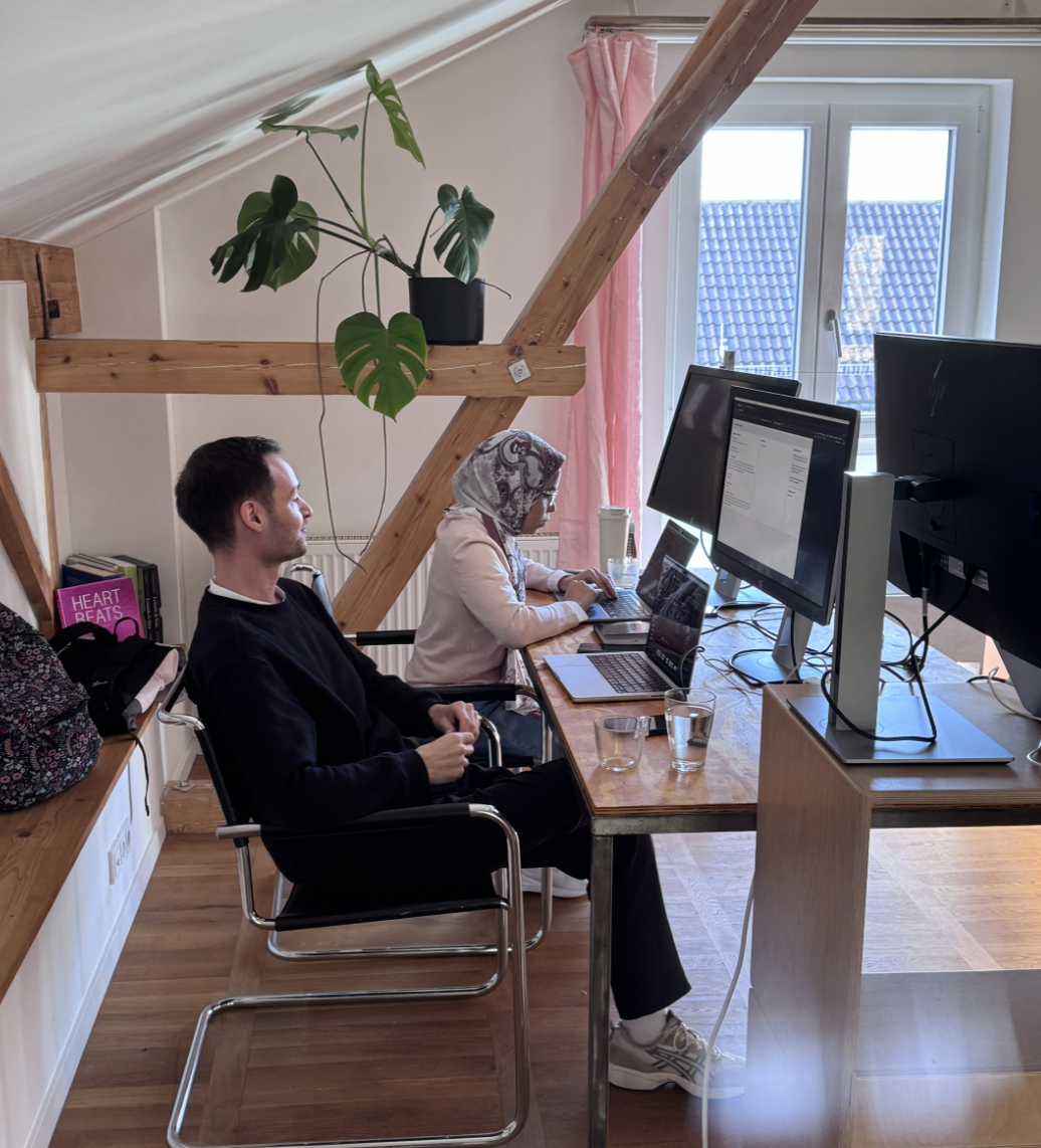 Two F24 hackathon participants focused on the product at a shared workstation.
